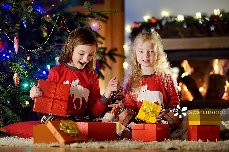 圣诞节前夕，快乐的小妹妹们穿着圣诞睡衣在舒适黑暗的客厅壁炉旁玩耍图片素材