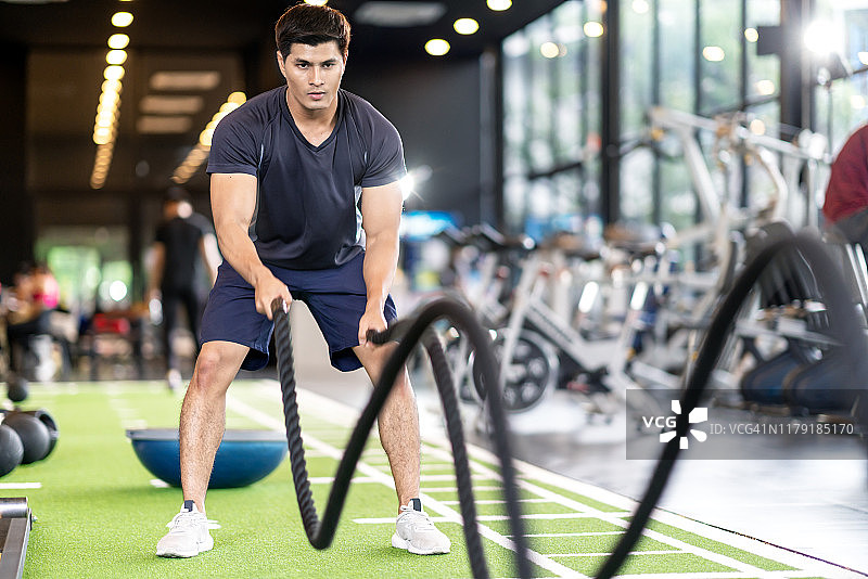 运动的亚洲人运动与战斗绳在体育馆的绿色地板上。强壮的男性决定她的室内锻炼耐力和建立肌肉的身体。运动员格斗绳训练概念。图片素材