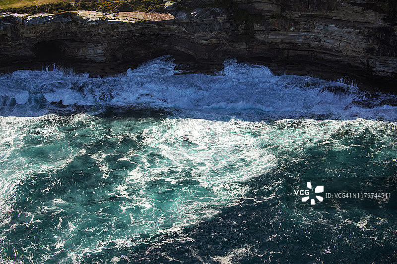 蓝绿色的海浪冲击着岩石嶙峋的海岸线图片素材