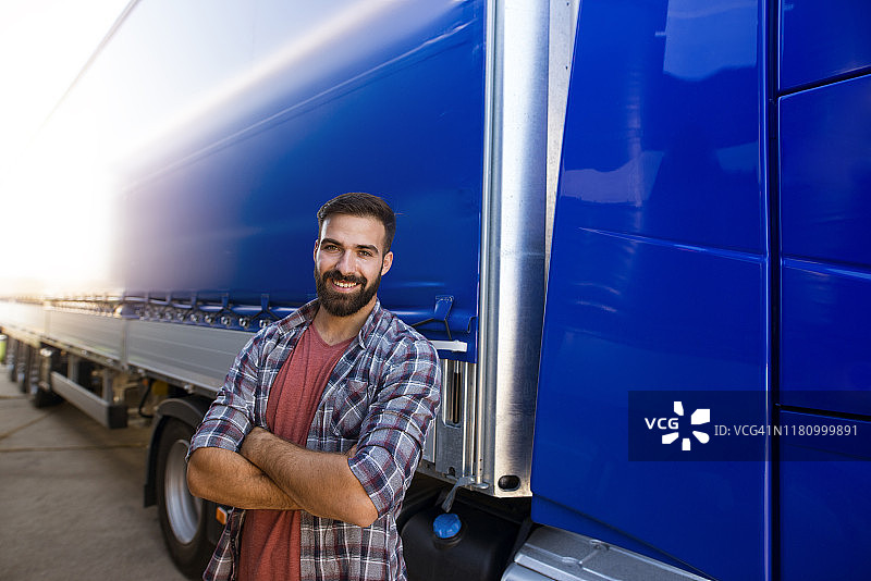 肖像的职业中年胡子卡车司机在休闲衣服交叉双臂站在他的卡车。运输服务。图片素材