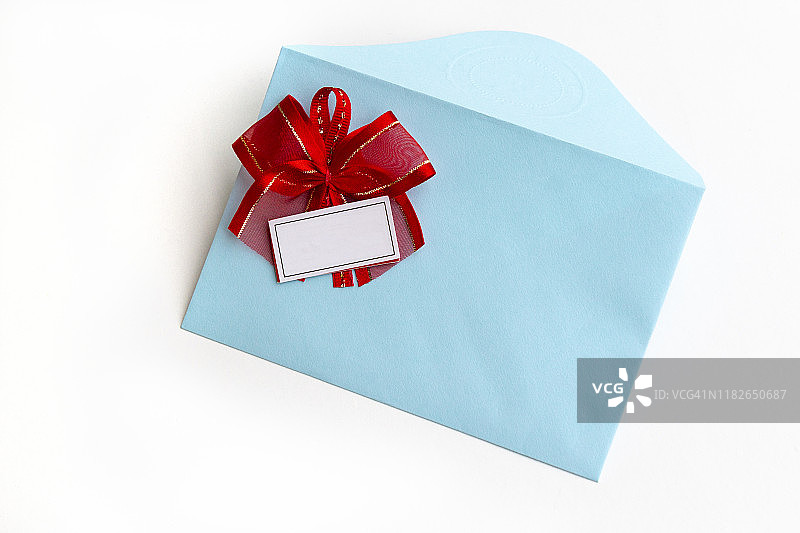 空白纸蓝色信封与红色缎带蝴蝶结，信为邮寄在白色的背景，平躺，俯视图。概念邮政服务或贺卡。图片素材