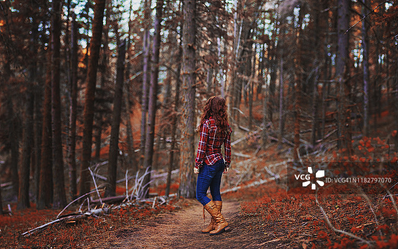后视图的年轻女子在红色格子衬衫，牛仔裤，和棕黄色靴子站在森林小径，秋天图片素材