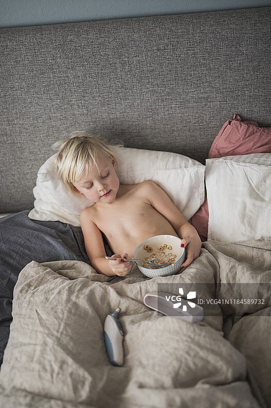 男孩躺在床上吃麦片图片素材