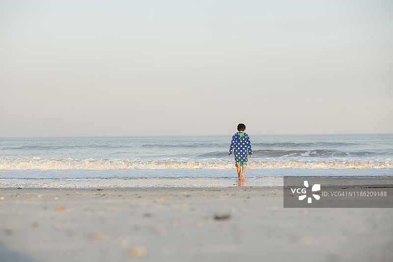 后视图的男孩走在海岸上对晴朗的天空日落图片素材