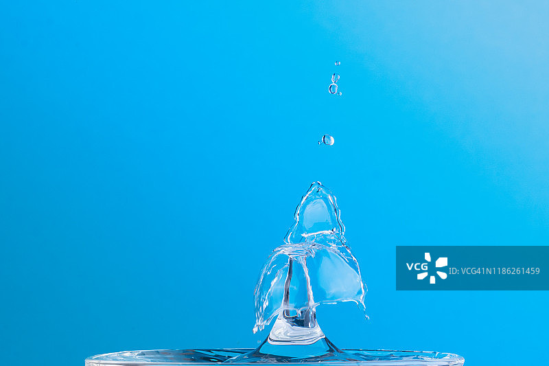 在玻璃杯里洒点水。两滴水的碰撞效果。蓝色背景。图片素材