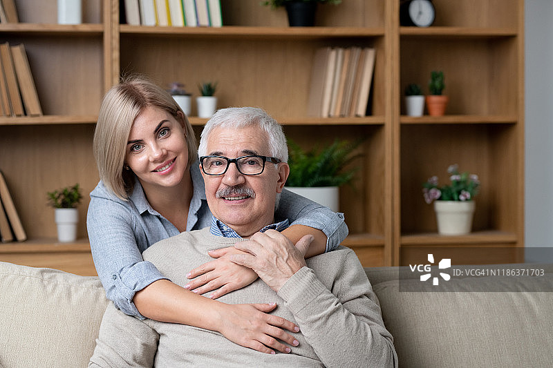在沙发上，快乐的金发女郎拥抱着她快乐的老父亲图片素材