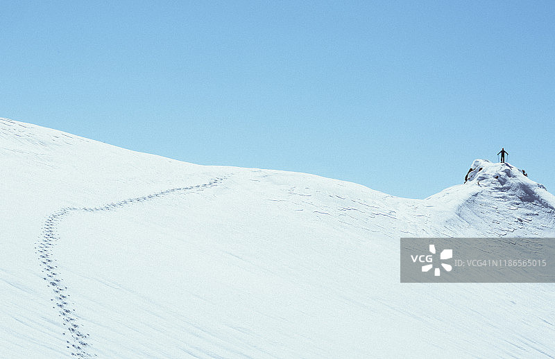 低角度远处的剪影远足者站在雪顶的悬崖上对抗晴朗的天空在冬天图片素材