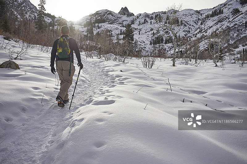 后视图的男性徒步旅行者与背包行走在白雪覆盖的山图片素材