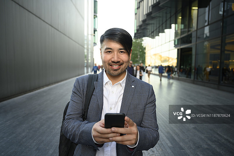 带着智能手机在户外微笑的中国商人图片素材