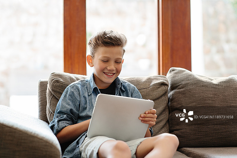 大笑的男孩坐在沙发上使用他的数字平板电脑图片素材