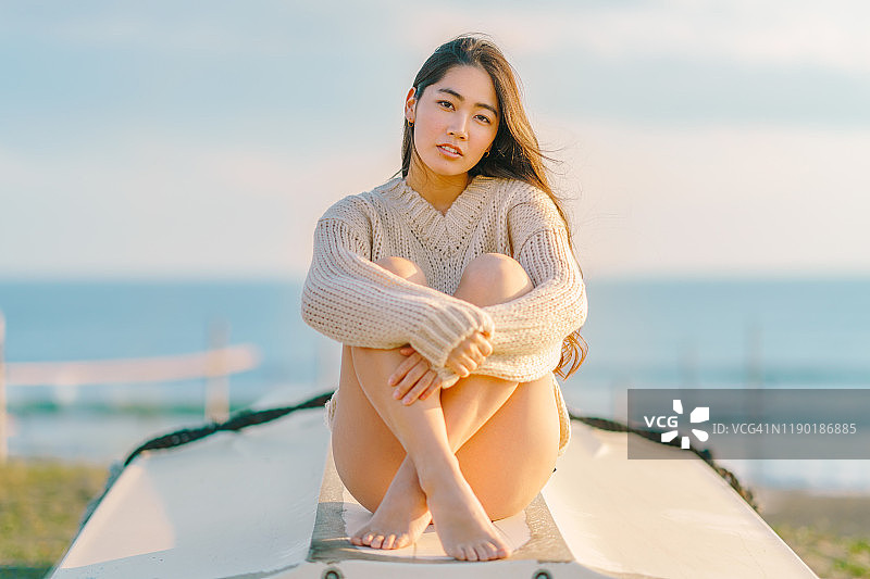 穿着针织毛衣和比基尼坐在小船上的年轻女子图片素材