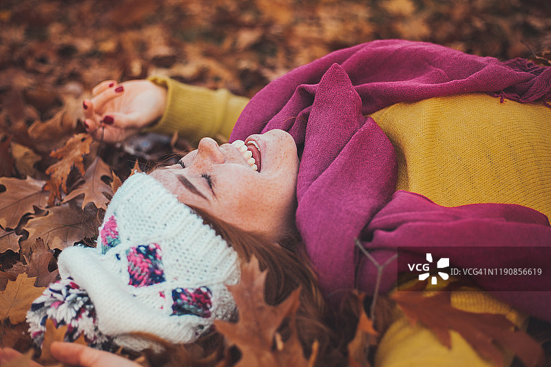 一个年轻的姜黄色女人的肖像躺在一堆秋叶上，穿着时髦的衣服图片素材