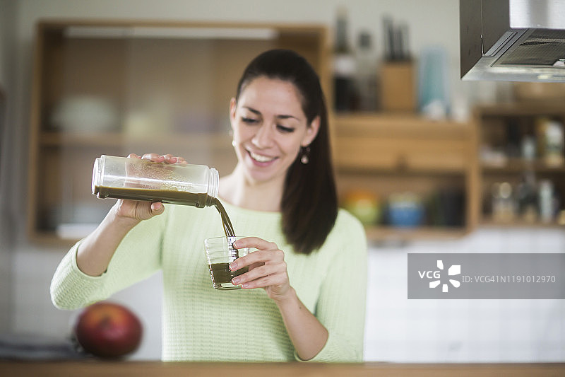 一个女人站在厨房里做健康的绿色果汁图片素材