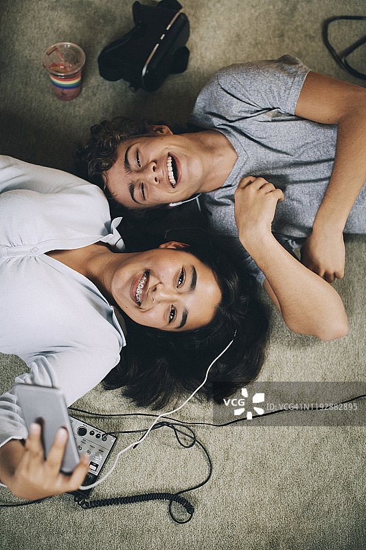 上图是快乐的朋友们躺在家里的地毯上一起听音乐图片素材