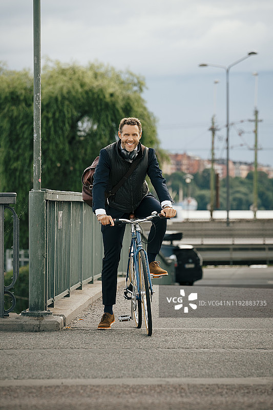 微笑的商人在城市的桥上骑自行车的肖像图片素材