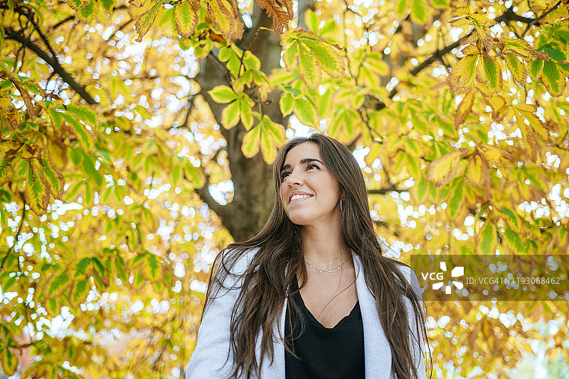 微笑的女人站在秋天的树下图片素材