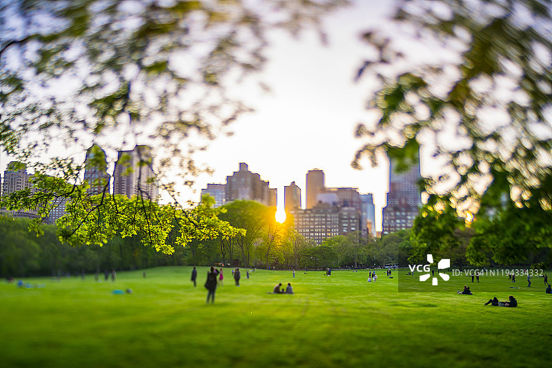 2019年5月11日，在美国纽约市中央公园，落日余晖照亮了公园内的建筑、绿树和人。图片素材