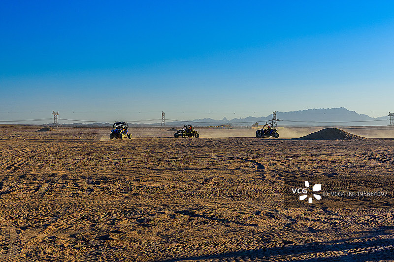 日落时分，埃及赫尔加达市附近的阿拉伯沙漠中，陌生的人们驾驶着四轮马车进行狩猎旅行图片素材