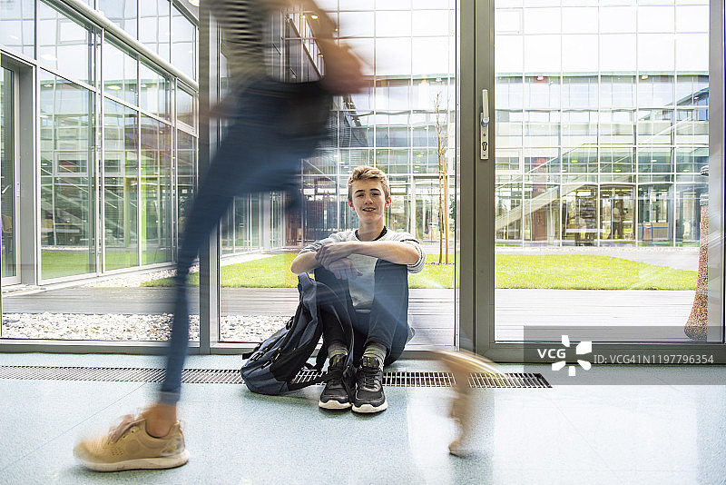 一个学生坐在走廊的地板上，微笑着图片素材