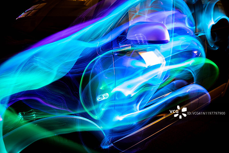 在夜晚，五颜六色的空气动力学灯光轨迹与汽车形状嬉戏。图片素材