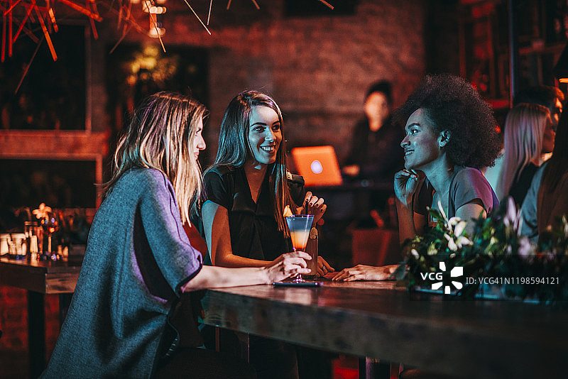 三个女性朋友在一个俱乐部的女孩之夜在桌子上聊天图片素材