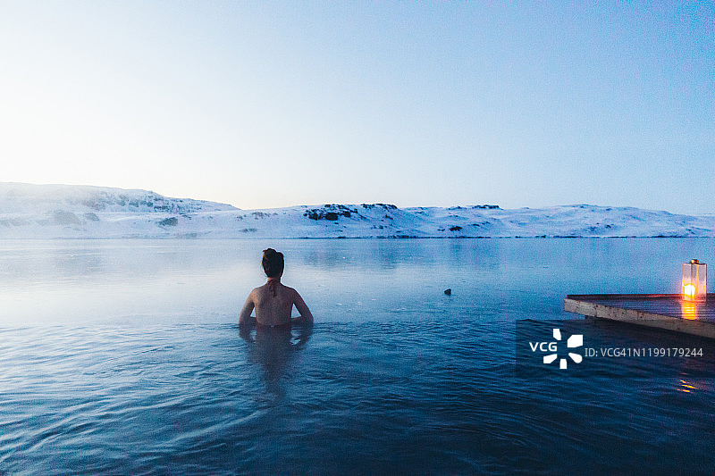 一名女子正在温泉池中沐浴，可以看到冰岛的雪山和冰湖图片素材