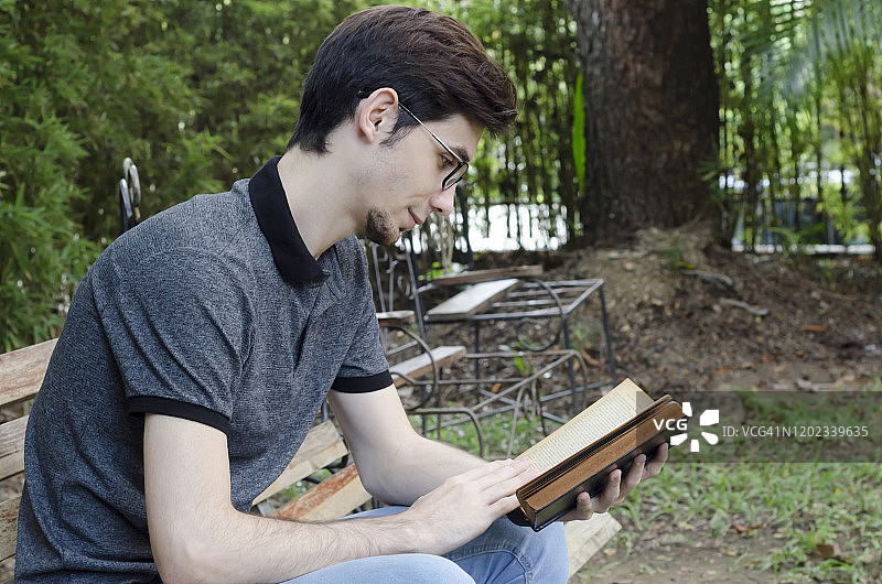 一个年轻人坐在花园里的长凳上看书图片素材