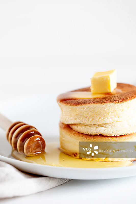 松软的日本soufflé薄烤饼，在浅白色的背景上涂上黄油和枫糖浆或蜂蜜酱图片素材