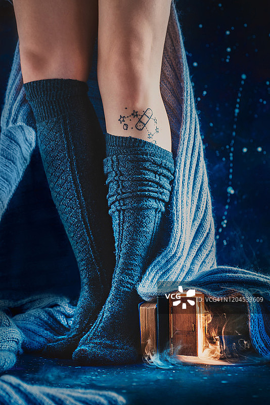 小门下的羊毛毯子和女人的腿在温暖的袜子，舒适的阅读冬天的概念图片素材