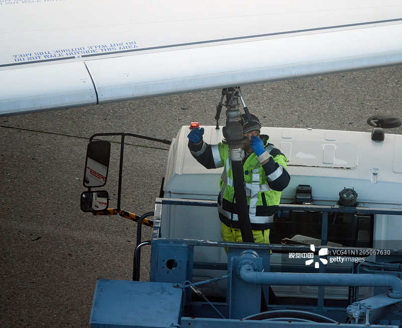 机场的加油站服务员将油罐车的软管与飞机机翼上的油罐喷嘴连接起来图片素材