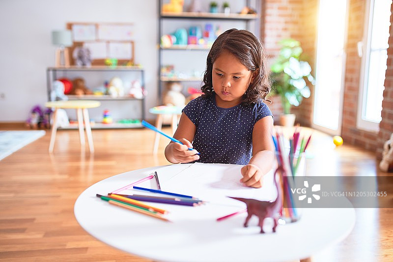美丽的蹒跚学步的小女孩在幼儿园用彩色铅笔画可爱的画图片素材
