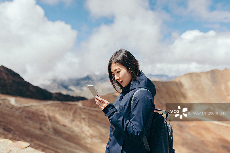 乌云密布的天空下，年轻女子在山上使用智能手机图片素材