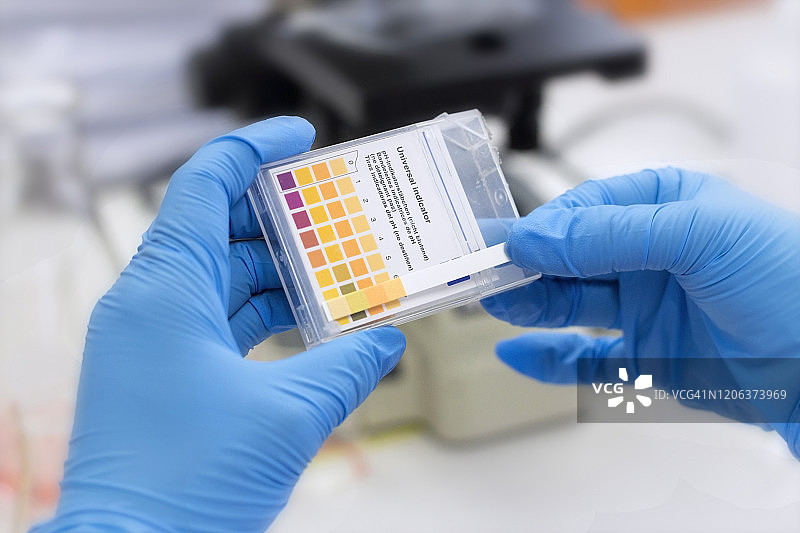 实验室概念;在化学实验室里，科学家手里拿着彩色石蕊试纸。图片素材