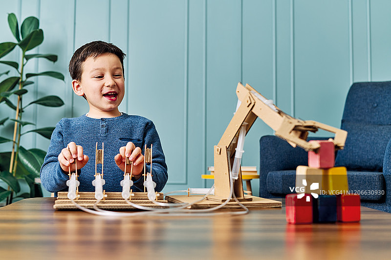 一个6-7岁的孩子发明了一个带纸板和注射器的机械手臂。机器人是他的家庭作业。他在小学时是个成功的学生。图片素材