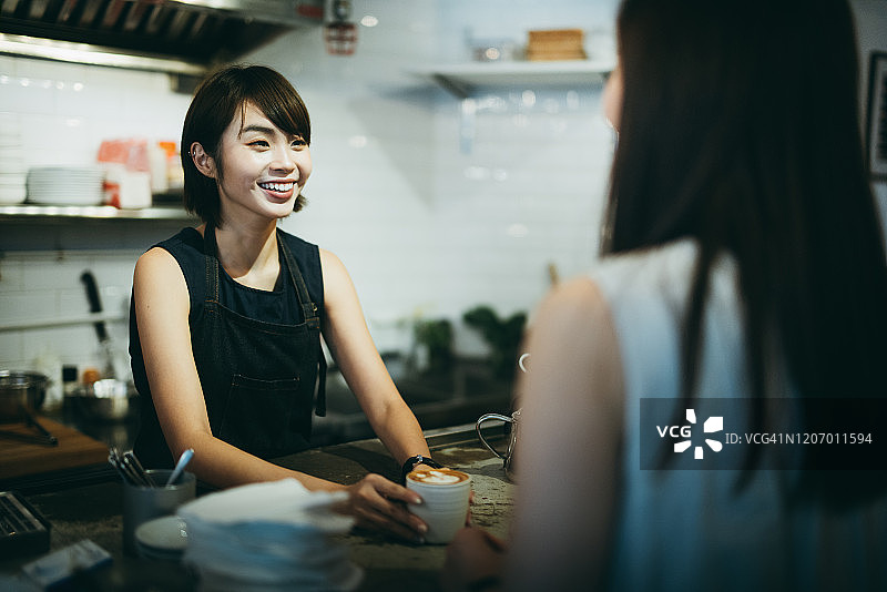 快乐年轻的亚洲女咖啡师在咖啡馆为顾客提供咖啡图片素材
