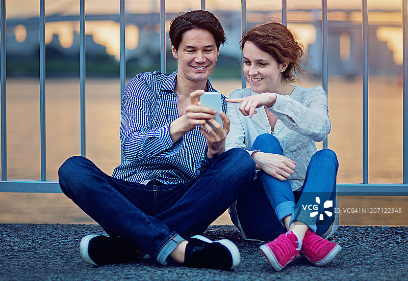 一对情侣正在东京市和彩虹桥前看手机图片素材