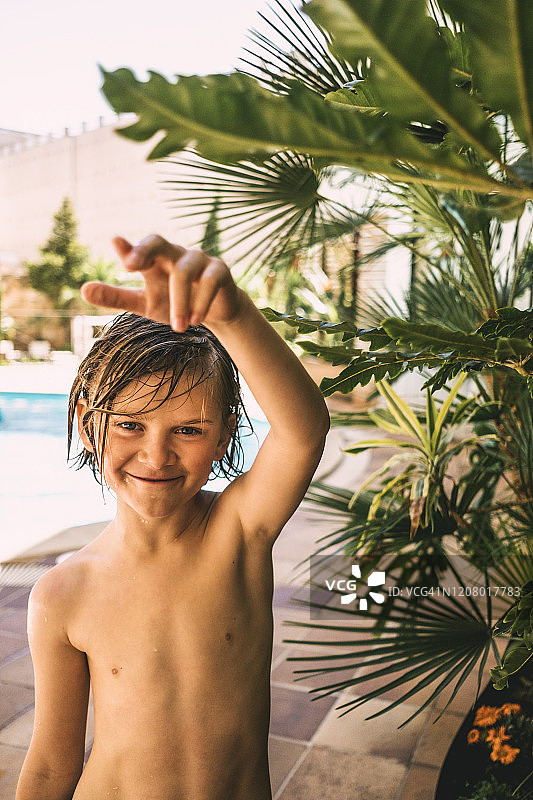赤裸上身的男孩站在植物对游泳池在度假村图片素材