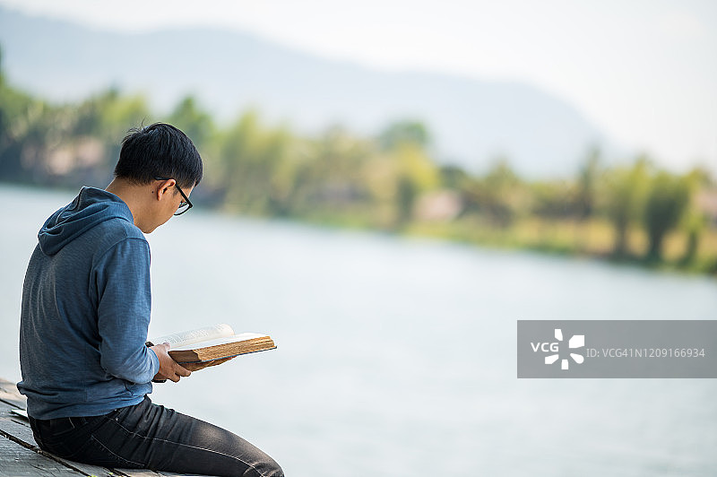 一个年轻人在假期里看书，喝咖啡，在新鲜自然的户外咖啡馆放松时光。图片素材