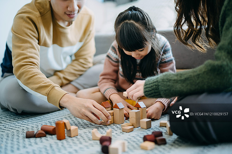 快乐的亚洲父母坐在客厅的地板上，与女儿一起玩木制积木图片素材