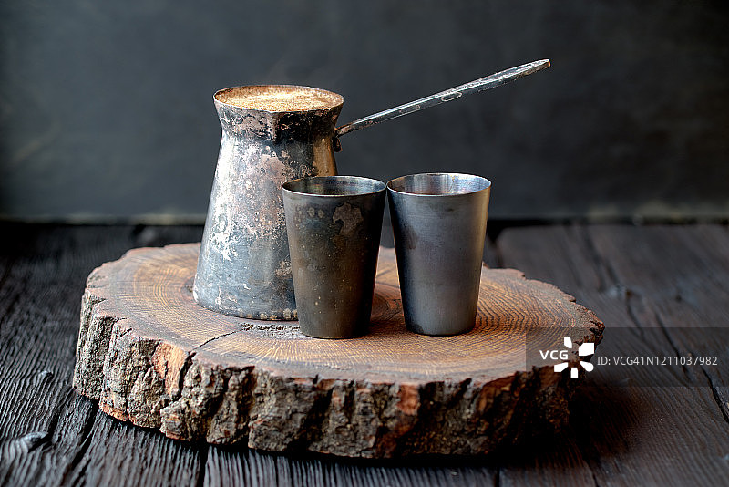 深色橡木桌子上，黑色背景，复古闪亮的铜土耳其咖啡壶和杯子图片素材