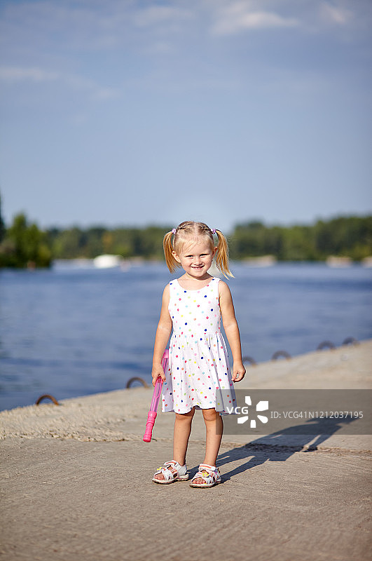 可爱的孩子穿着白色连衣裙在户外摆姿势。女孩很开心。小女孩在公园里。暑假或春假图片素材