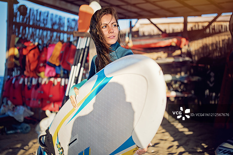 一名年轻女子在海上帆板冲浪后举着冲浪板的肖像图片素材