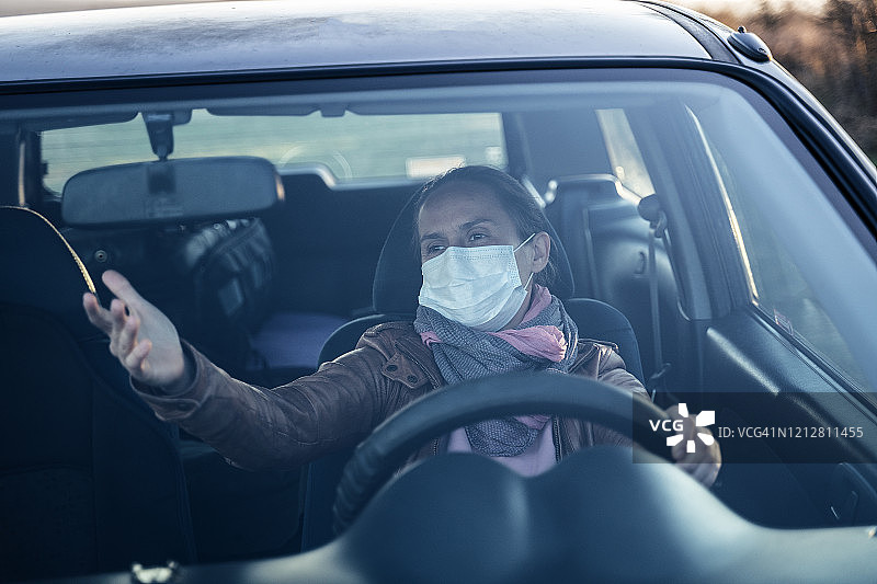活跃的年轻女子开车去上班。戴着保护面罩开车。图片素材