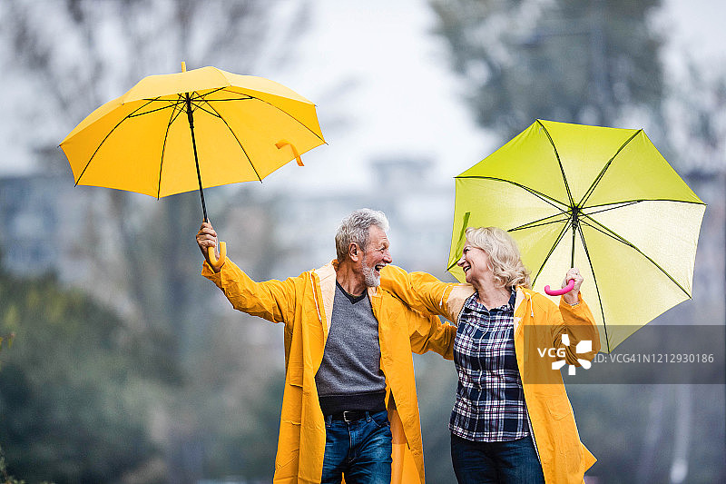 快乐的成熟夫妇穿着黄色雨衣，在大自然中拿着雨伞玩。图片素材
