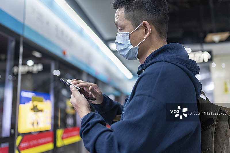 一名亚洲男子在等地铁时擦拭手机屏幕图片素材