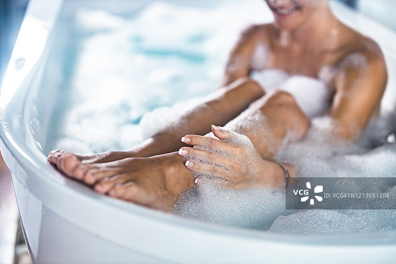 一个女人洗她的腿在泡沫浴的特写。图片素材