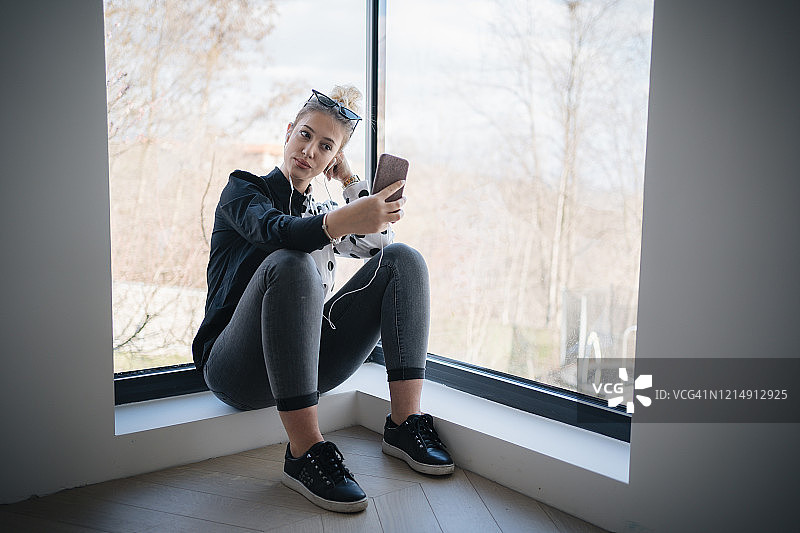 放松的女孩坐在靠近窗户的家里和短信的电话图片素材