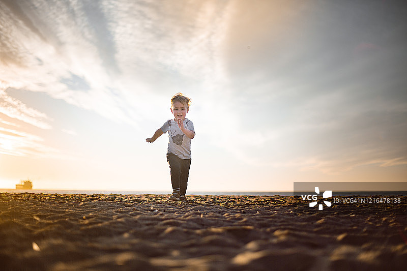 日落时分，男孩在海滩上朝着照相机跑去图片素材