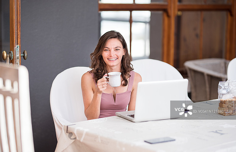 女人微笑着，拿着一个杯子坐在电脑前图片素材