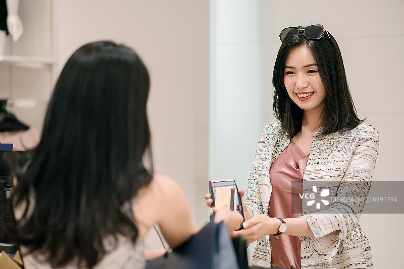 亚洲华人女性在服装店用信用卡进行非接触式支付购买新衣服图片素材